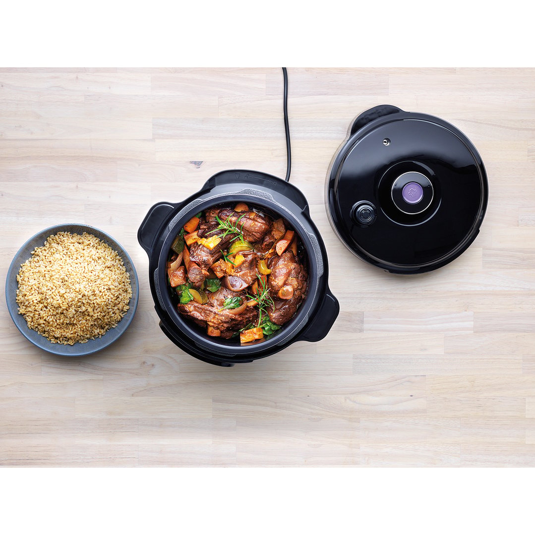 Overhead view of a black multicooker with stew and a bowl of rice
