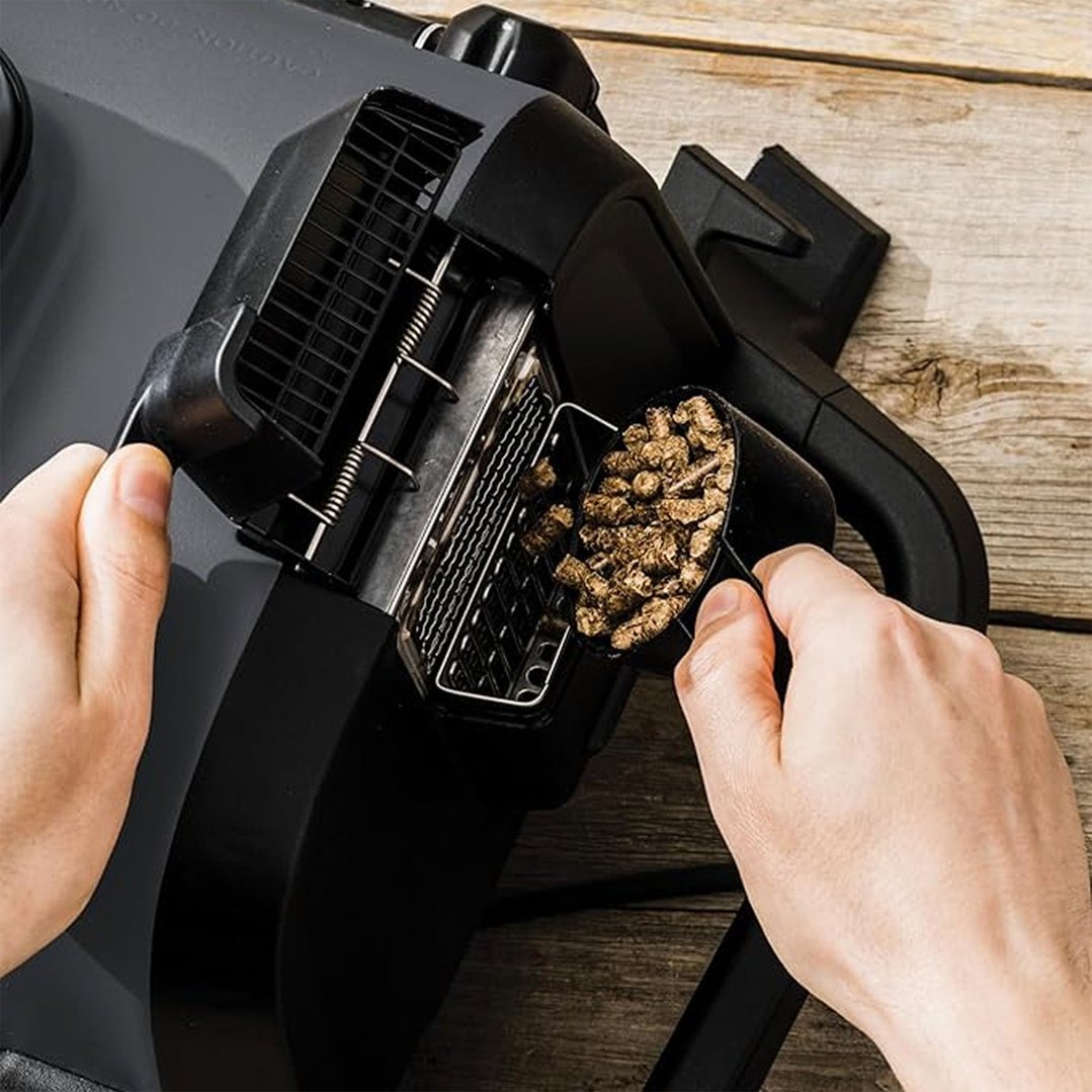 Hands pouring wood pellets into the hopper of a Ninja Woodfire Grill