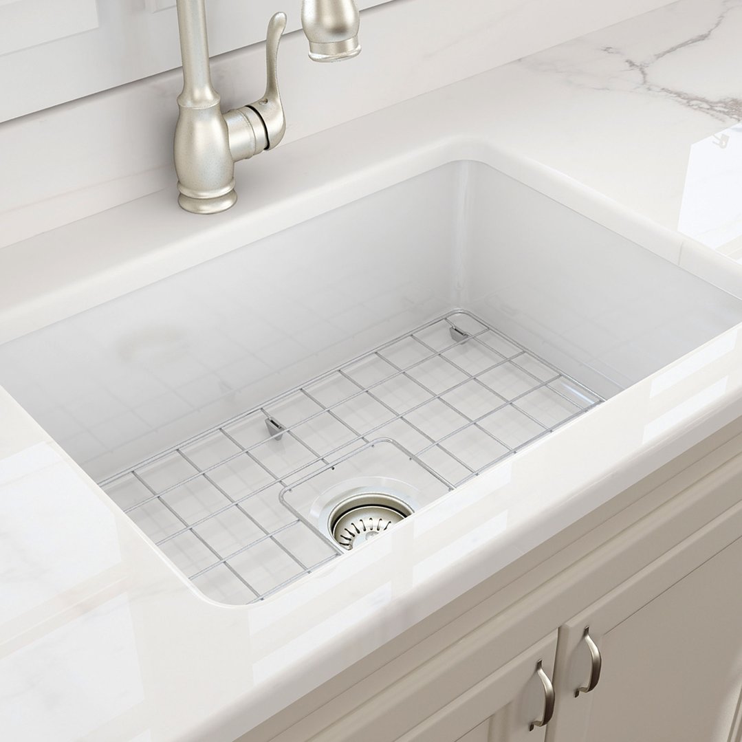 White fireclay sink with a metal grid in a kitchen setting