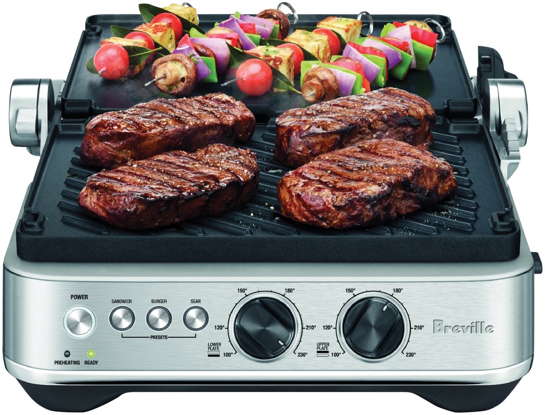 Breville Sear & Press Grill cooking steaks and vegetable skewers on a white background