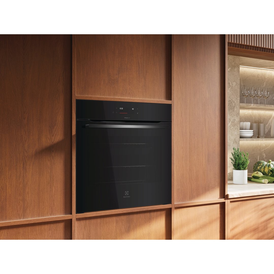 Built-in black oven with digital display in a wooden kitchen cabinet