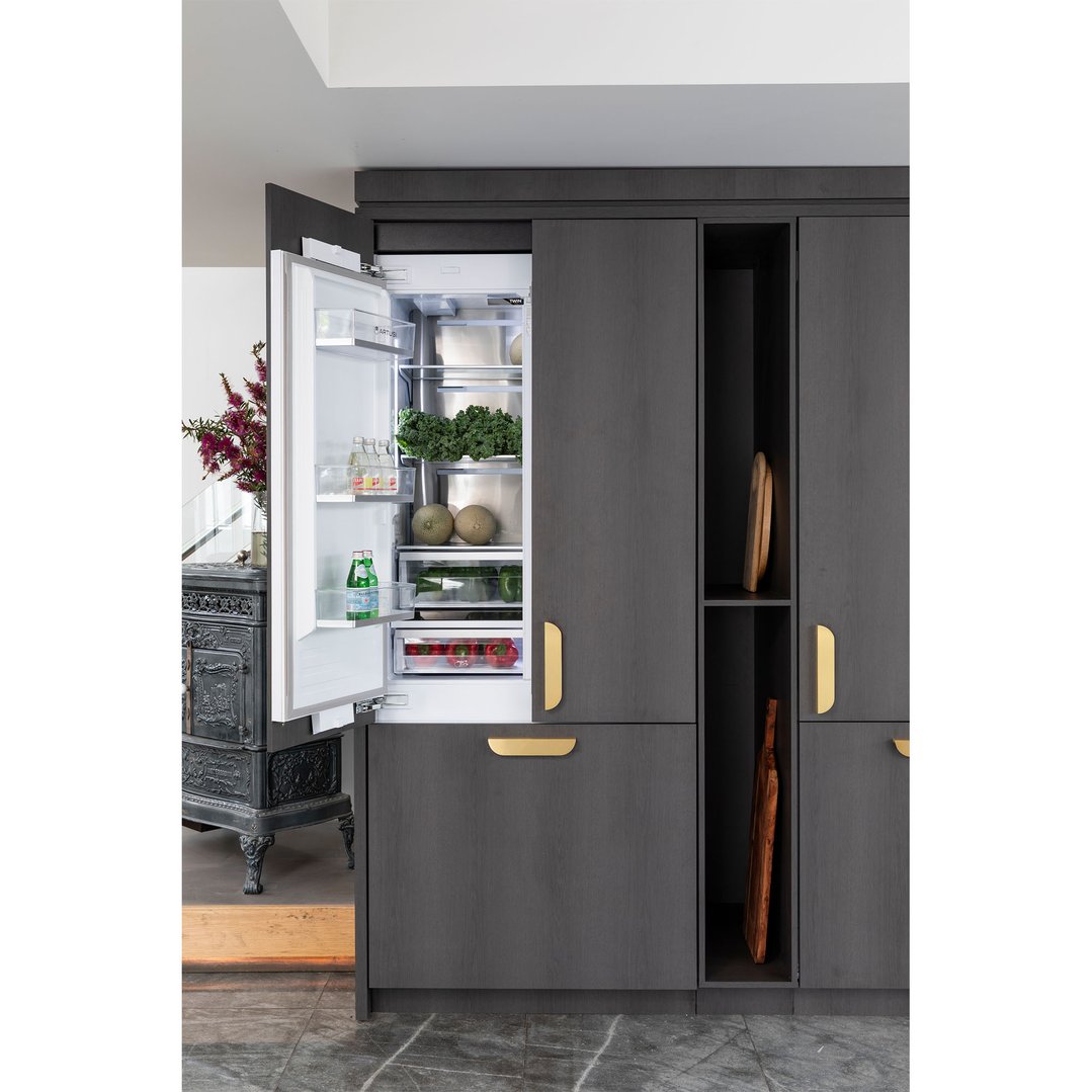 Open integrated French door fridge filled with fresh produce in a dark kitchen