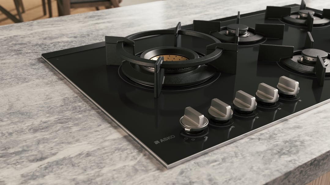 Black glass gas cooktop with five burners and control knobs on a marble countertop