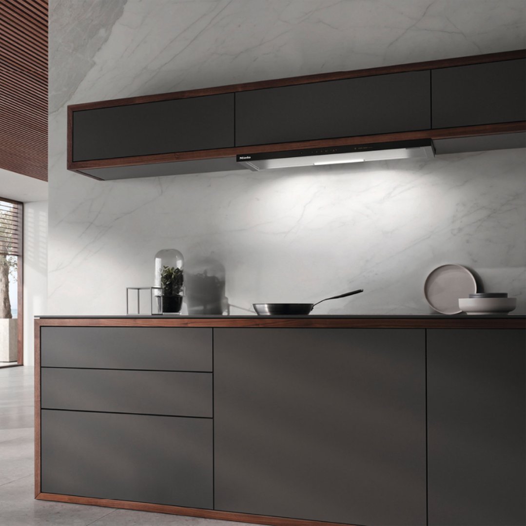 A rangehood integrated into dark cabinetry above a kitchen counter with a pan