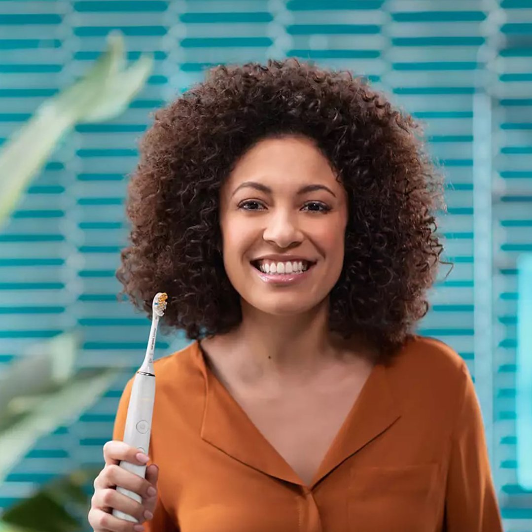 Smiling woman holding a white electric toothbrush in a bathroom setting