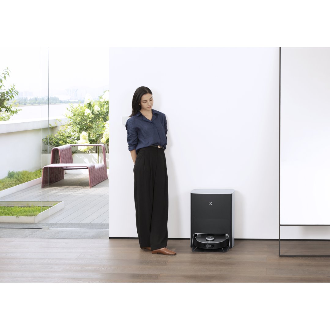 Woman standing next to a robotic vacuum in a modern room with outdoor patio