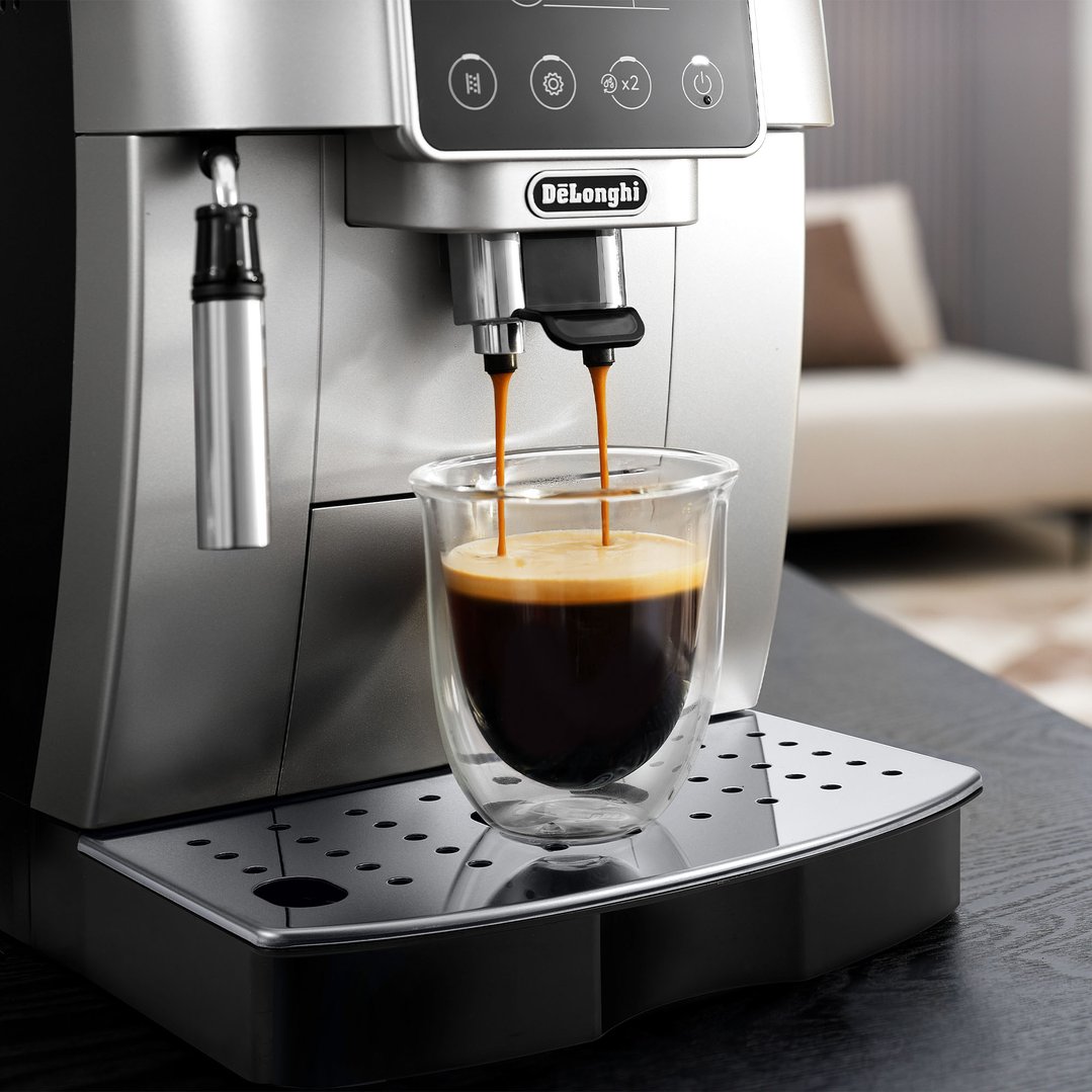A DELONGHI coffee machine dispensing espresso into a glass cup on a dark table