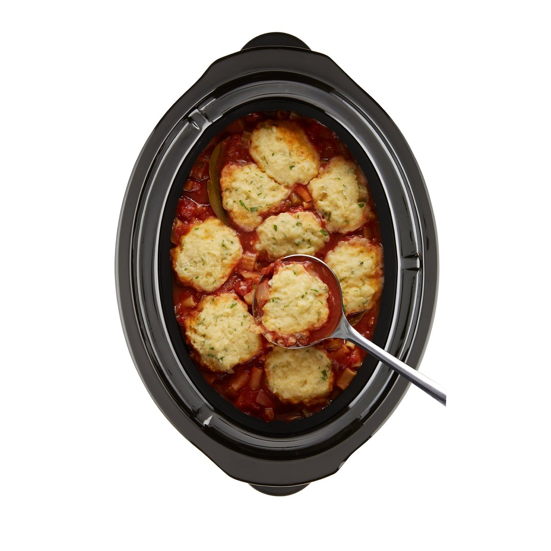 Overhead view of a slow cooker filled with stew and dumplings, with a spoon