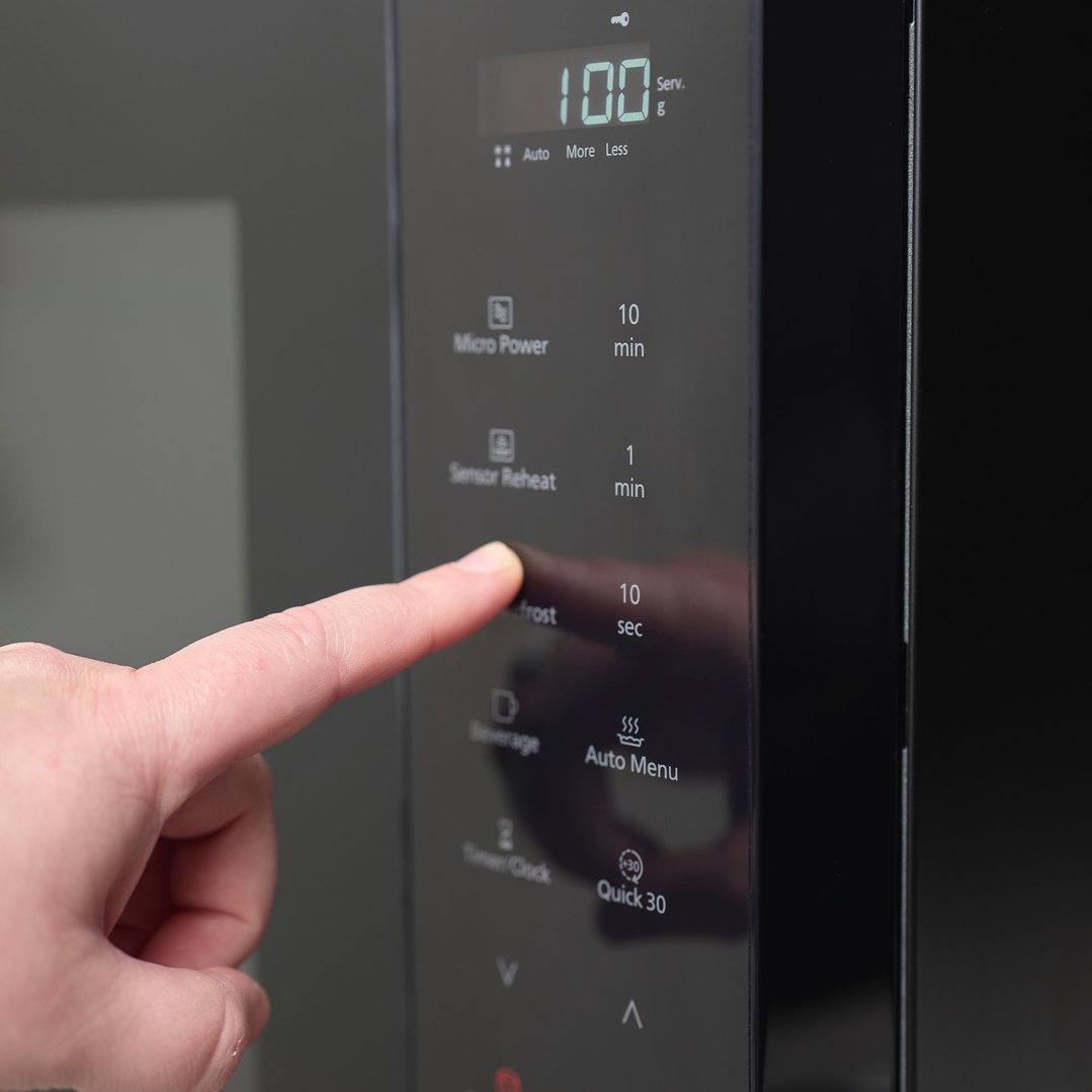 A person's finger pressing a button on a black microwave control panel