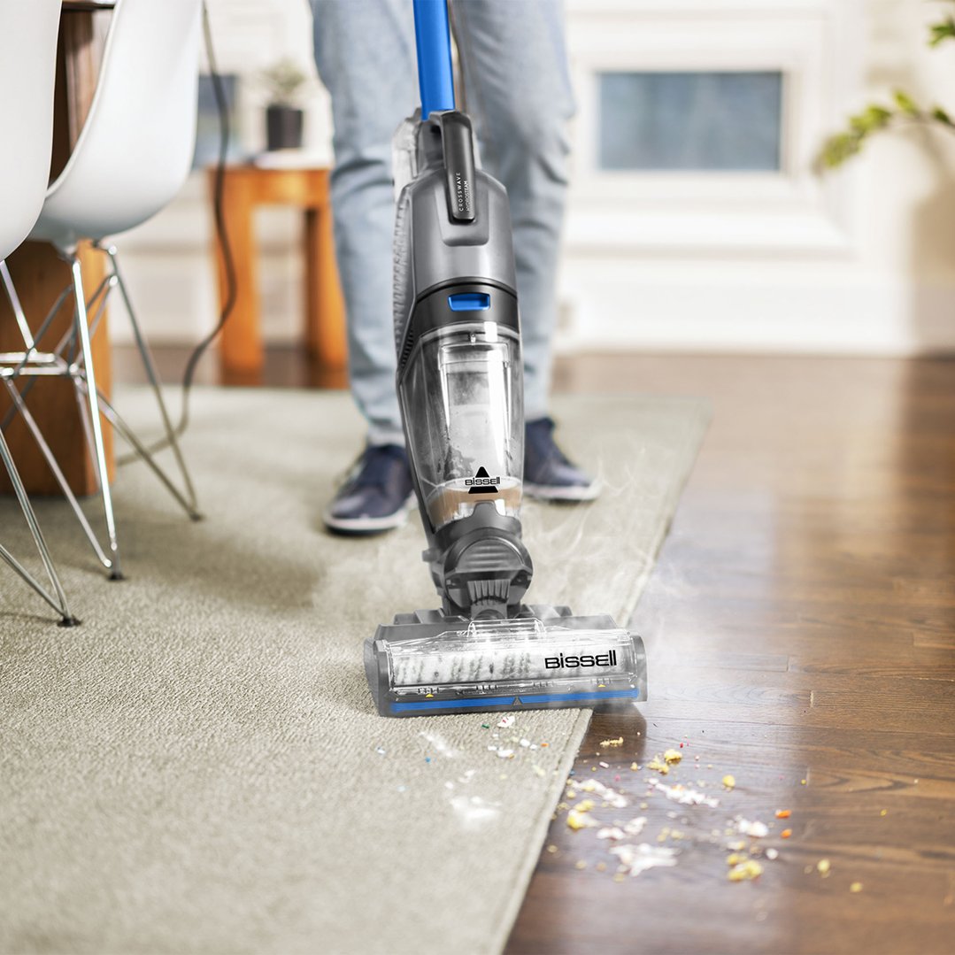Person using a BISSELL CrossWave HydroSteam vacuum cleaner on carpet and wood floor