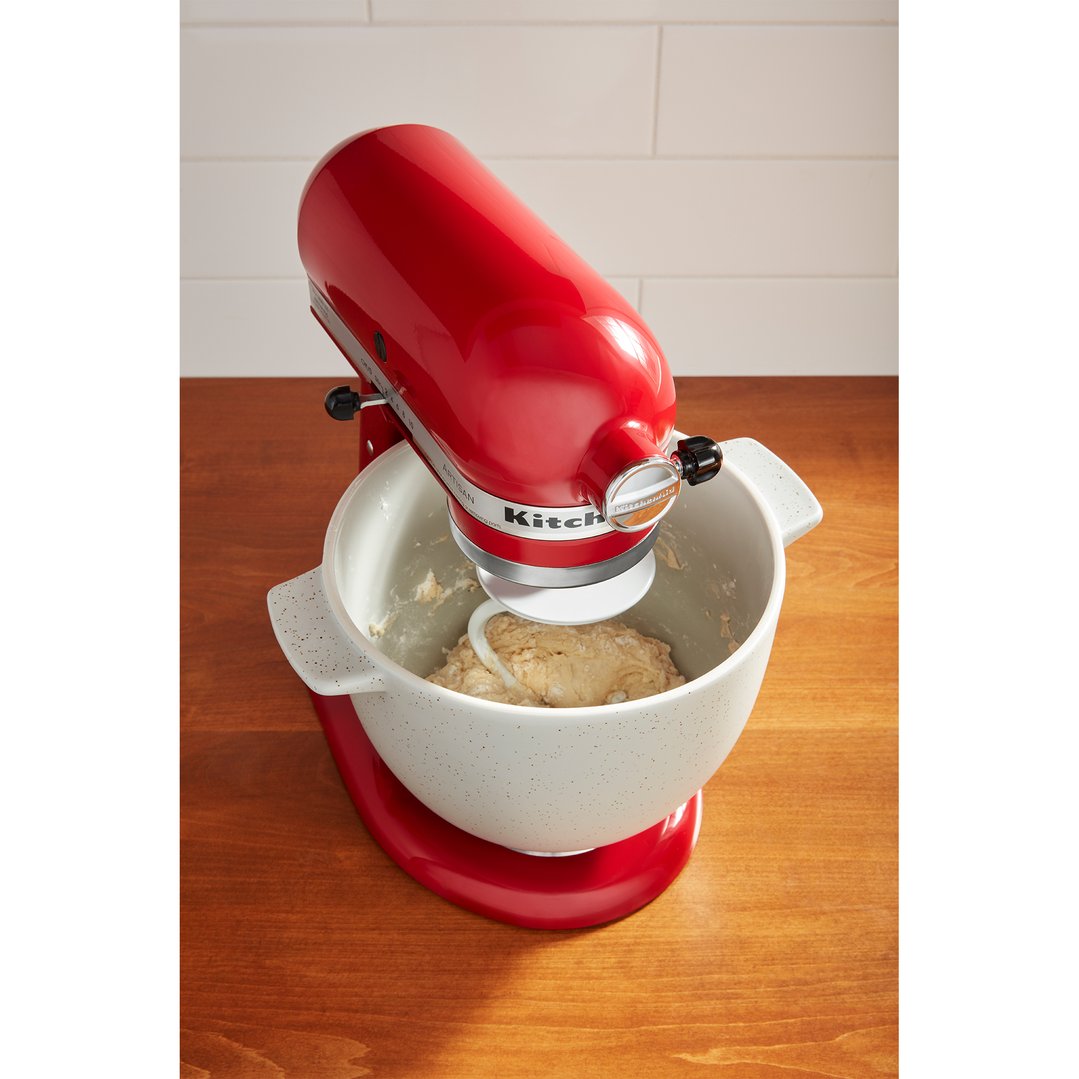 Red KitchenAid stand mixer with a white bowl mixing dough on a wooden surface