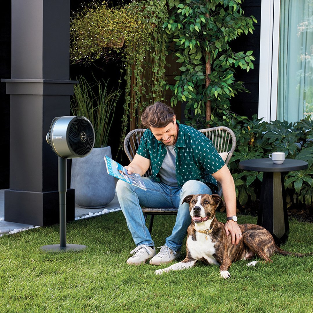 Man reading a magazine with his dog and a Shark fan on a stand