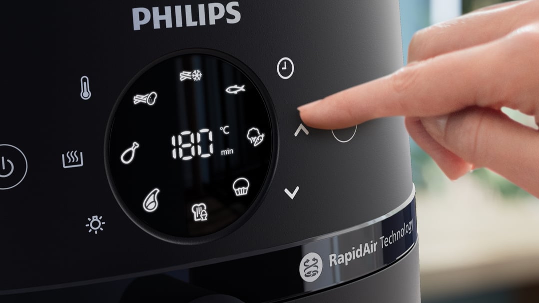 A hand adjusts the settings on a PHILIPS airfryer's digital display