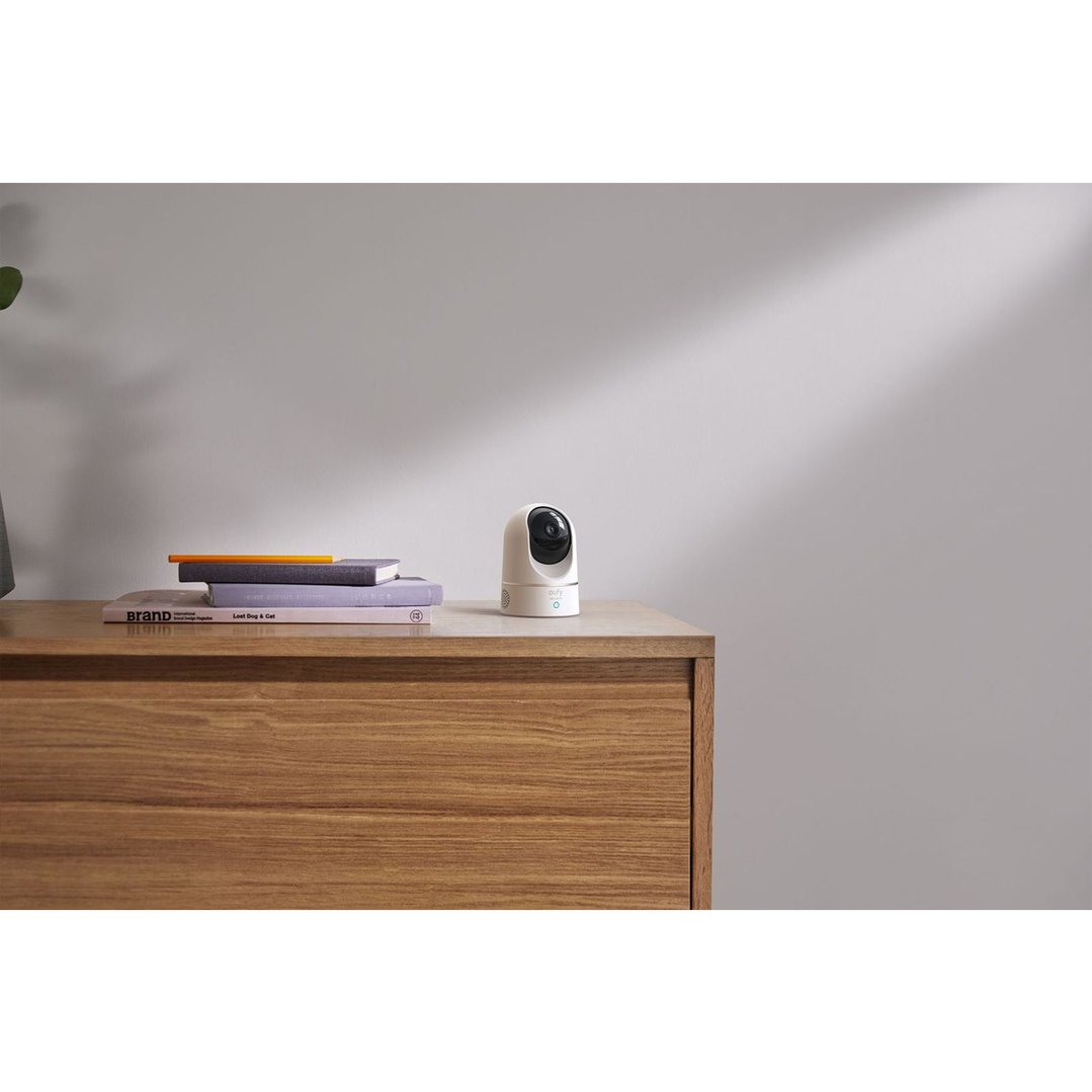A white security camera on a wooden dresser next to books