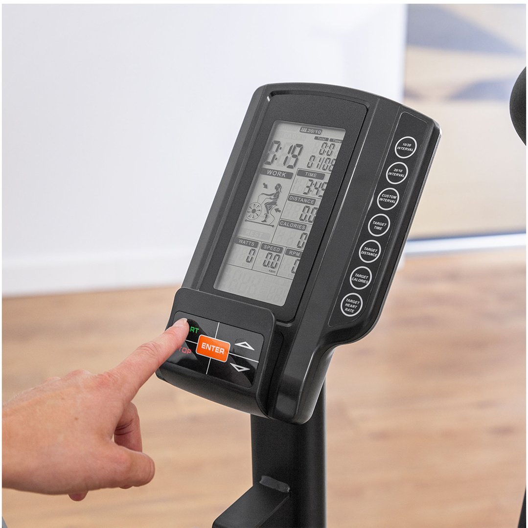 A hand pressing the start button on the exercise bike's console