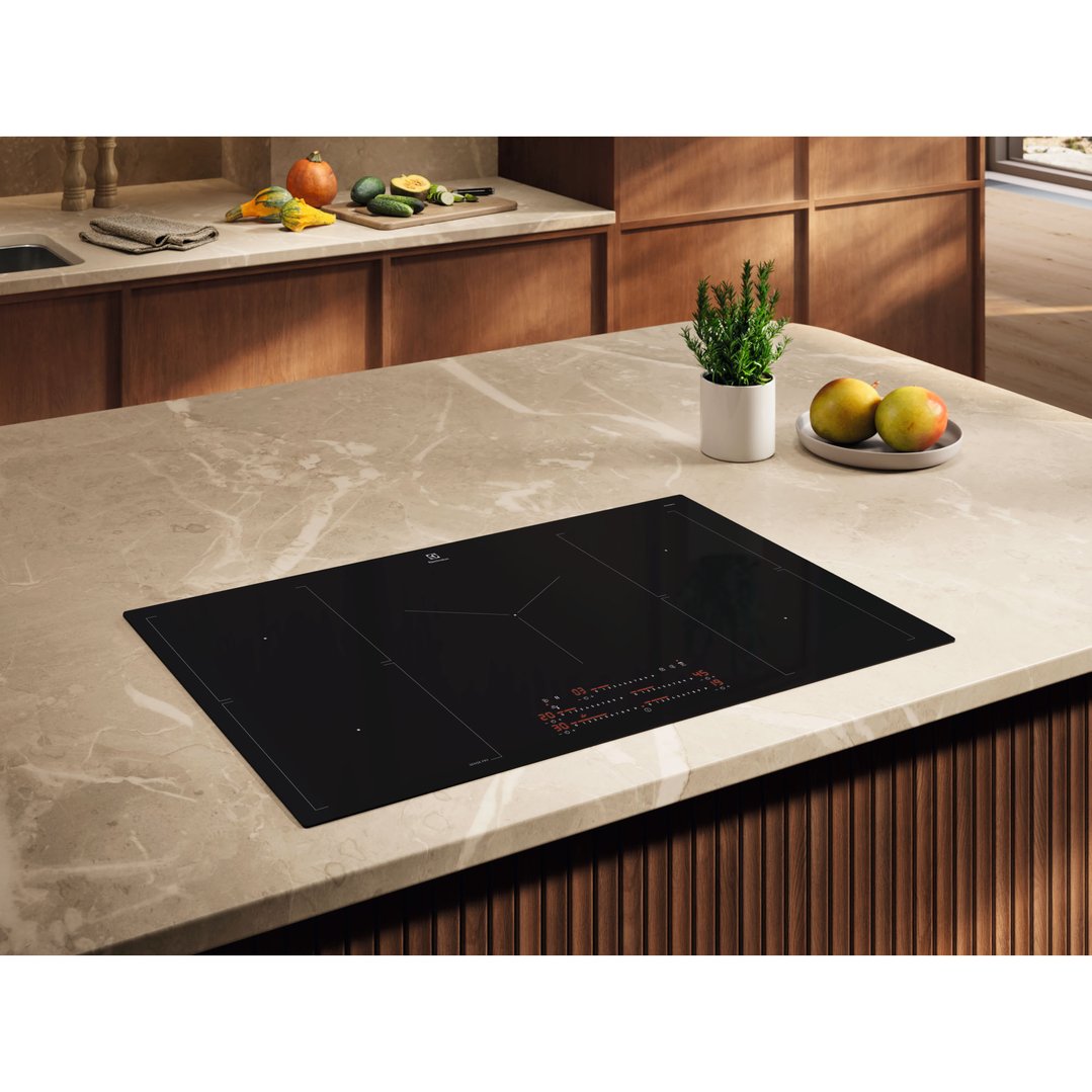 Black induction cooktop built into a light marble kitchen island with vegetables