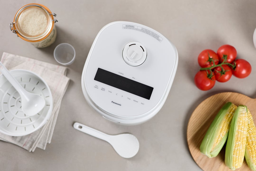 Overhead view of a white rice cooker with cooking ingredients on a grey surface