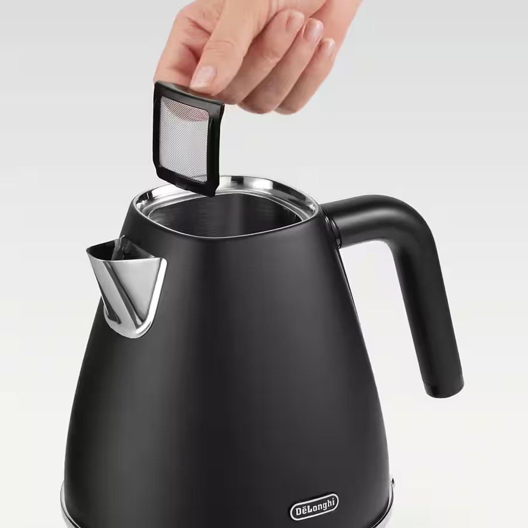 A hand removing the filter from a black DeLonghi kettle