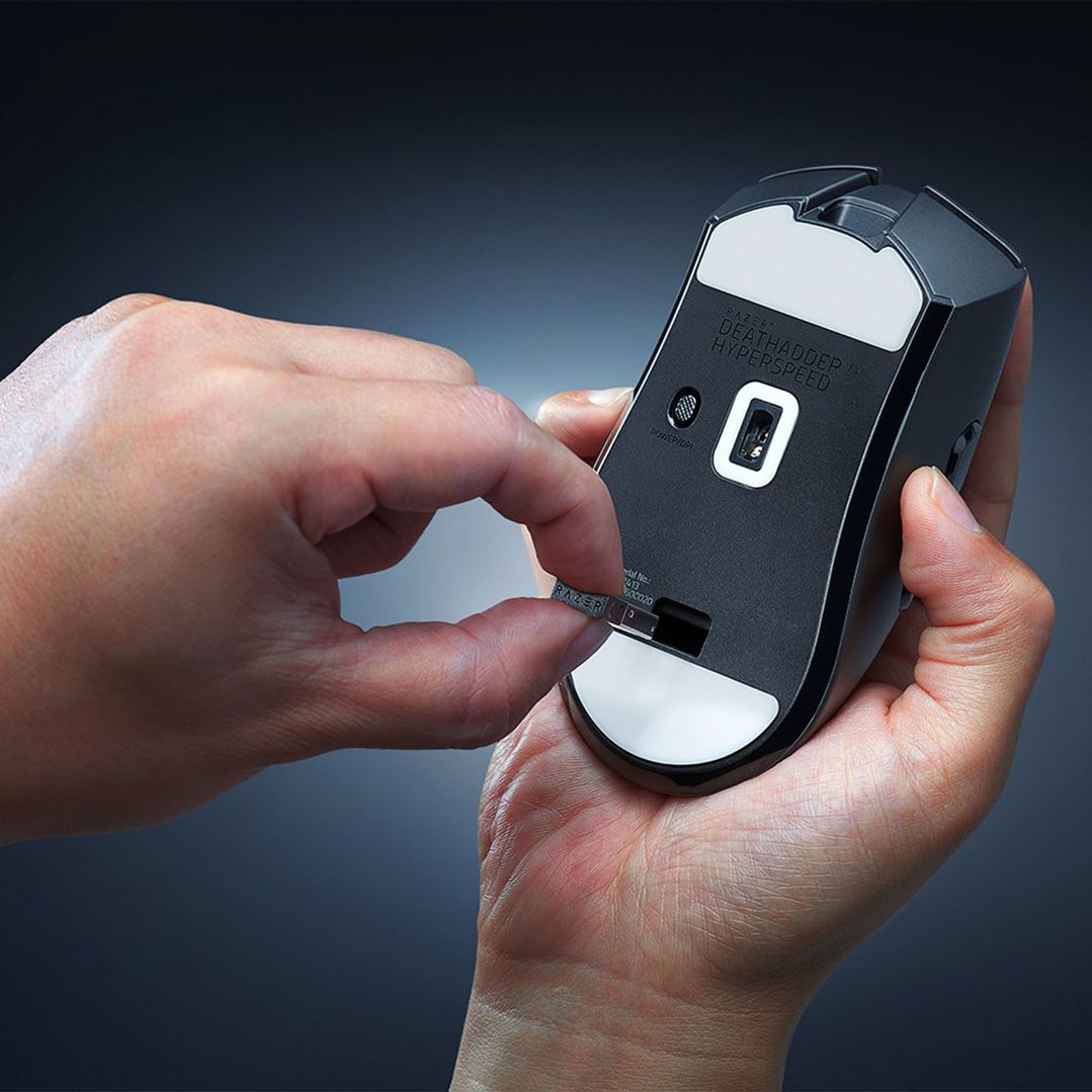 Hands inserting a USB dongle into the underside of a black gaming mouse