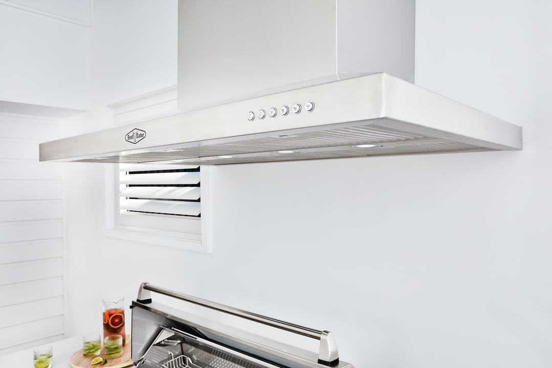 Stainless steel rangehood mounted above a grill with drinks on a wooden board