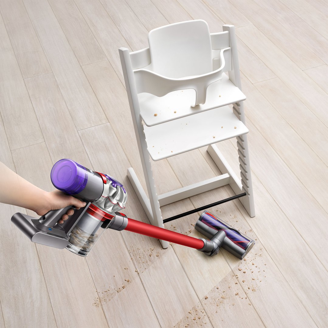 Hand using a Dyson hand stick vacuum to clean crumbs from a wooden floor