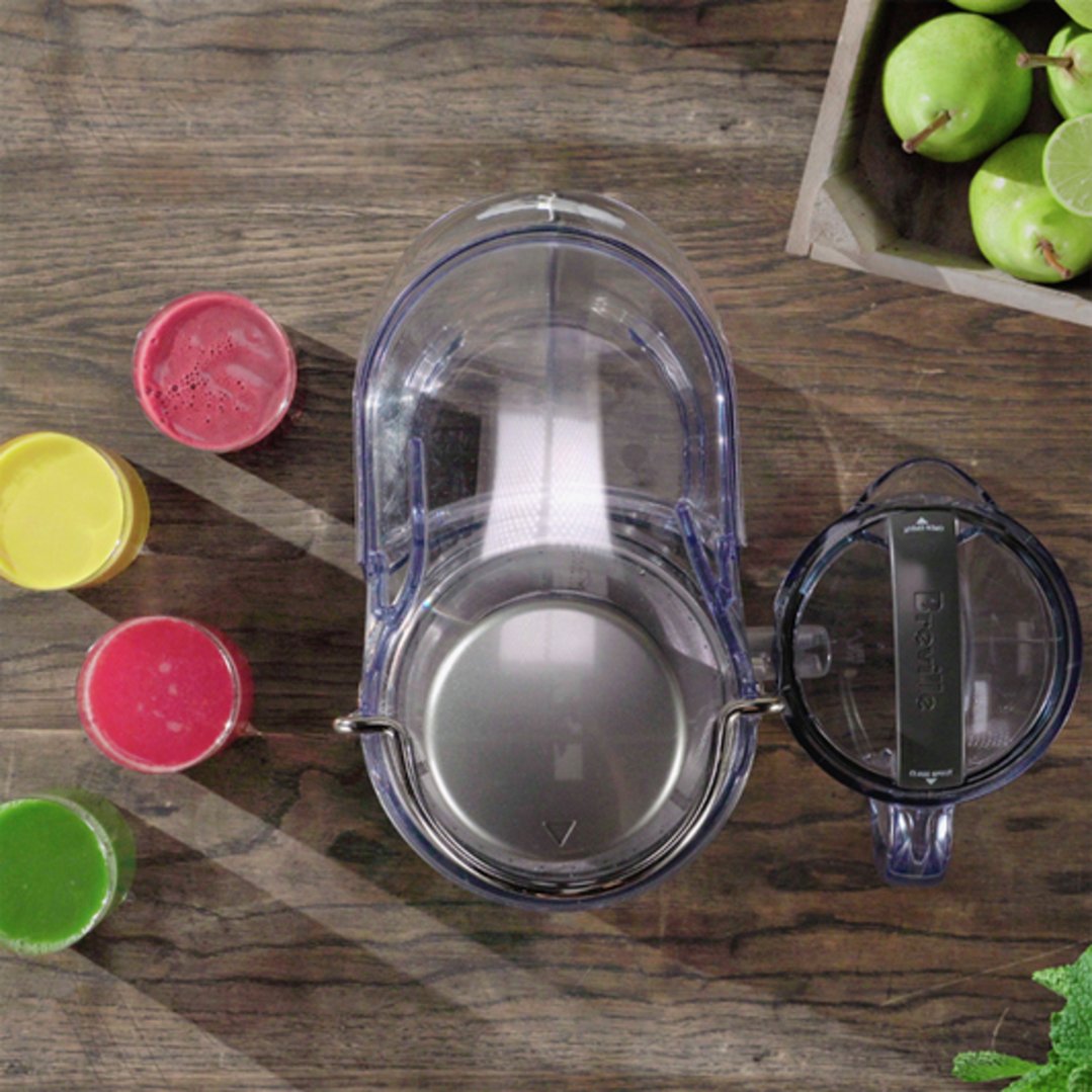 Overhead view of a Breville juicer with four glasses of juice and fruit