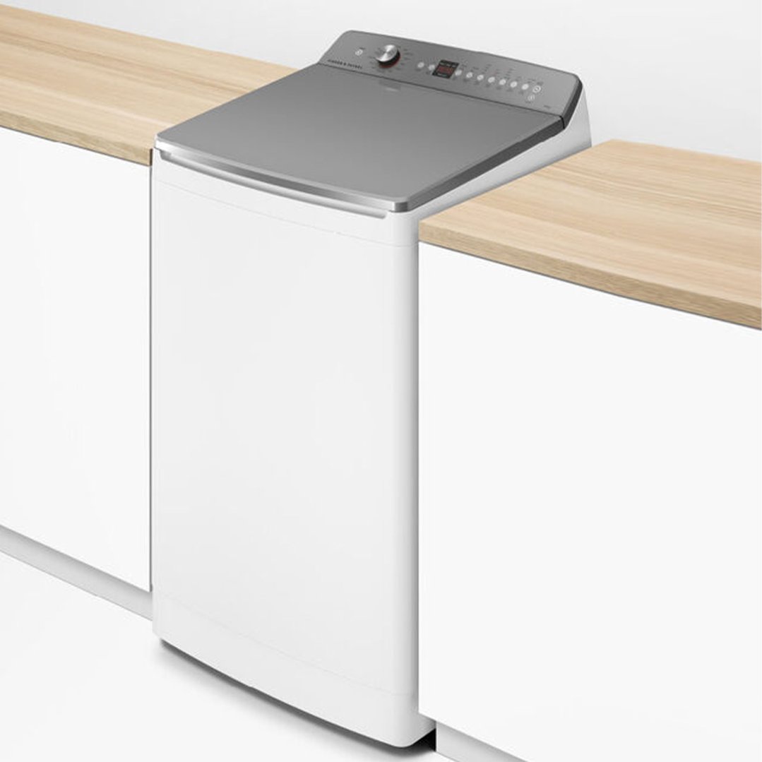 White top loader washing machine integrated into a light wood countertop