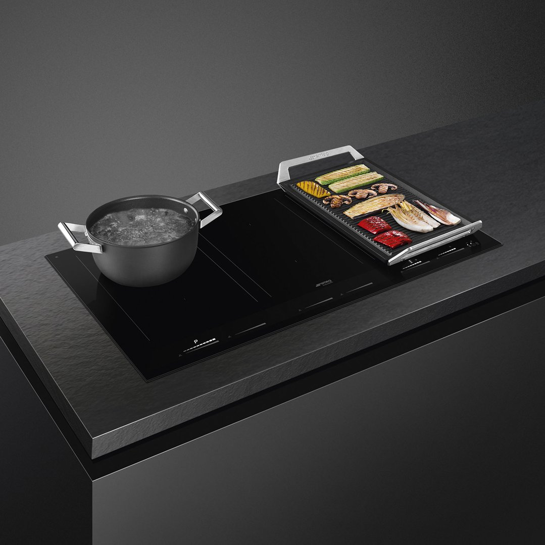 Induction cooktop with a pot of boiling water and a grill pan with vegetables