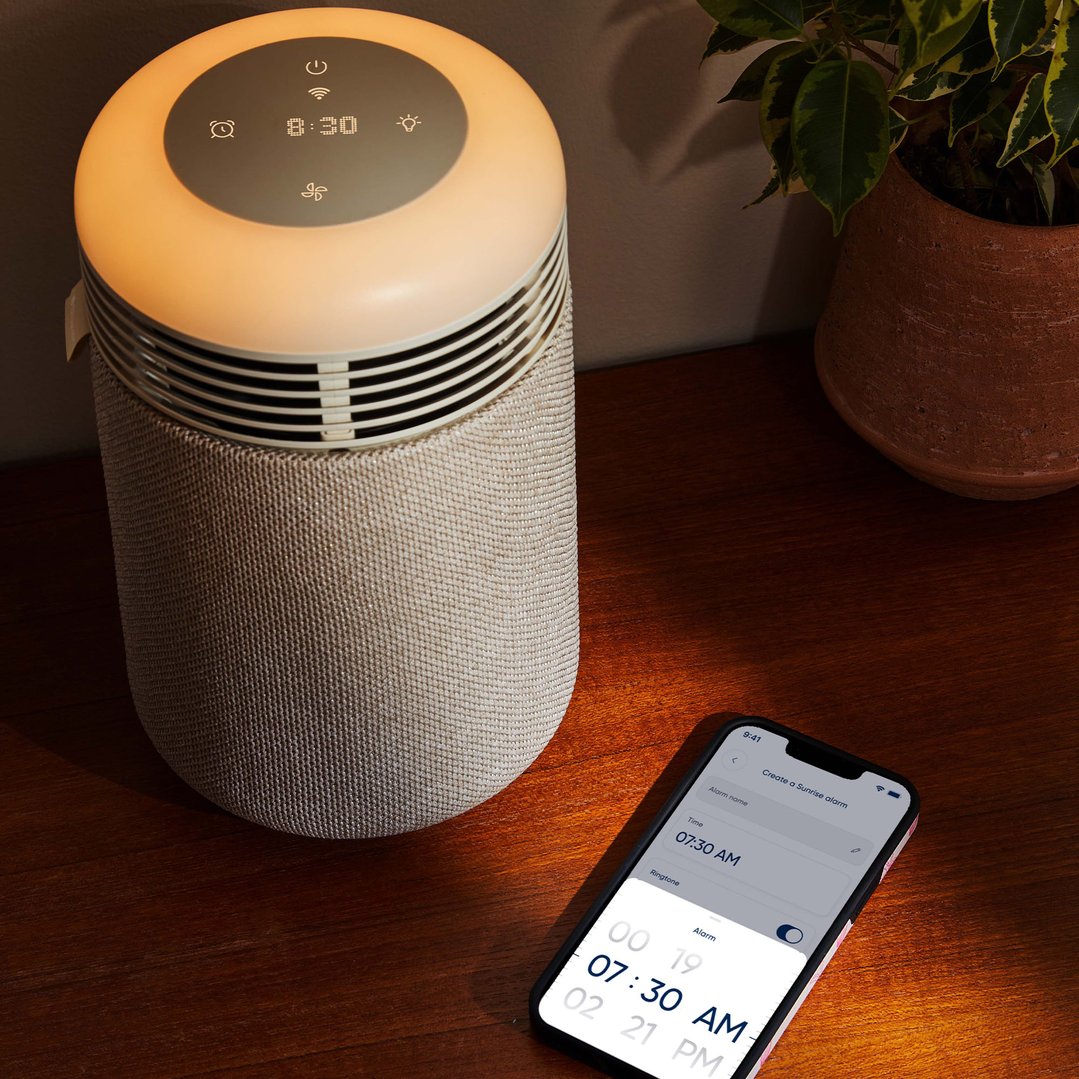 Beige air purifier with a digital clock and a smartphone on a wooden surface