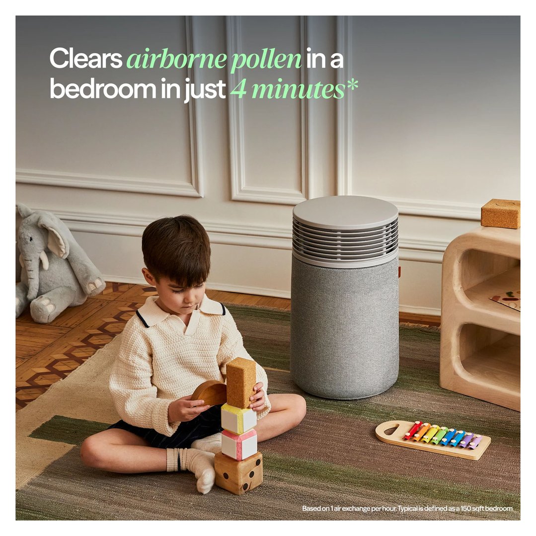 Child playing on a rug next to a Blueair air purifier in a bedroom