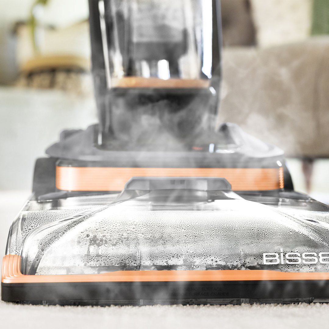 Close-up of a BISSELL vacuum cleaner head steaming on a white carpet