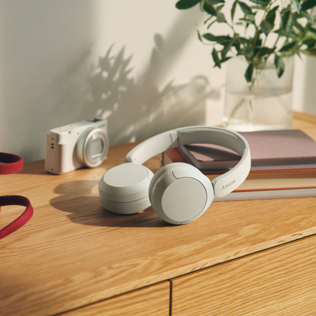 White Sony Wireless Headphones on a wooden surface with a camera and books