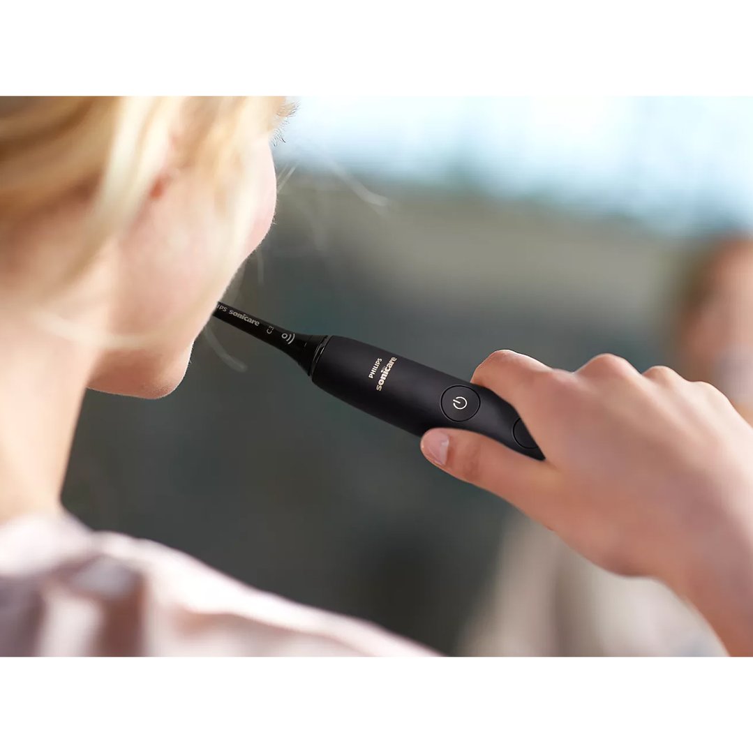 Person holding a black electric toothbrush to their mouth, ready to brush
