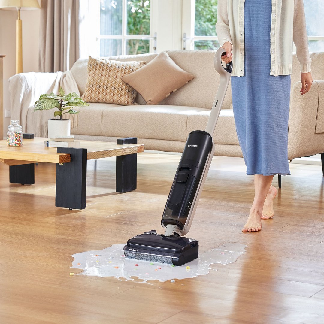 Woman using a TINECO vacuum cleaner to clean up a spill on a wooden floor