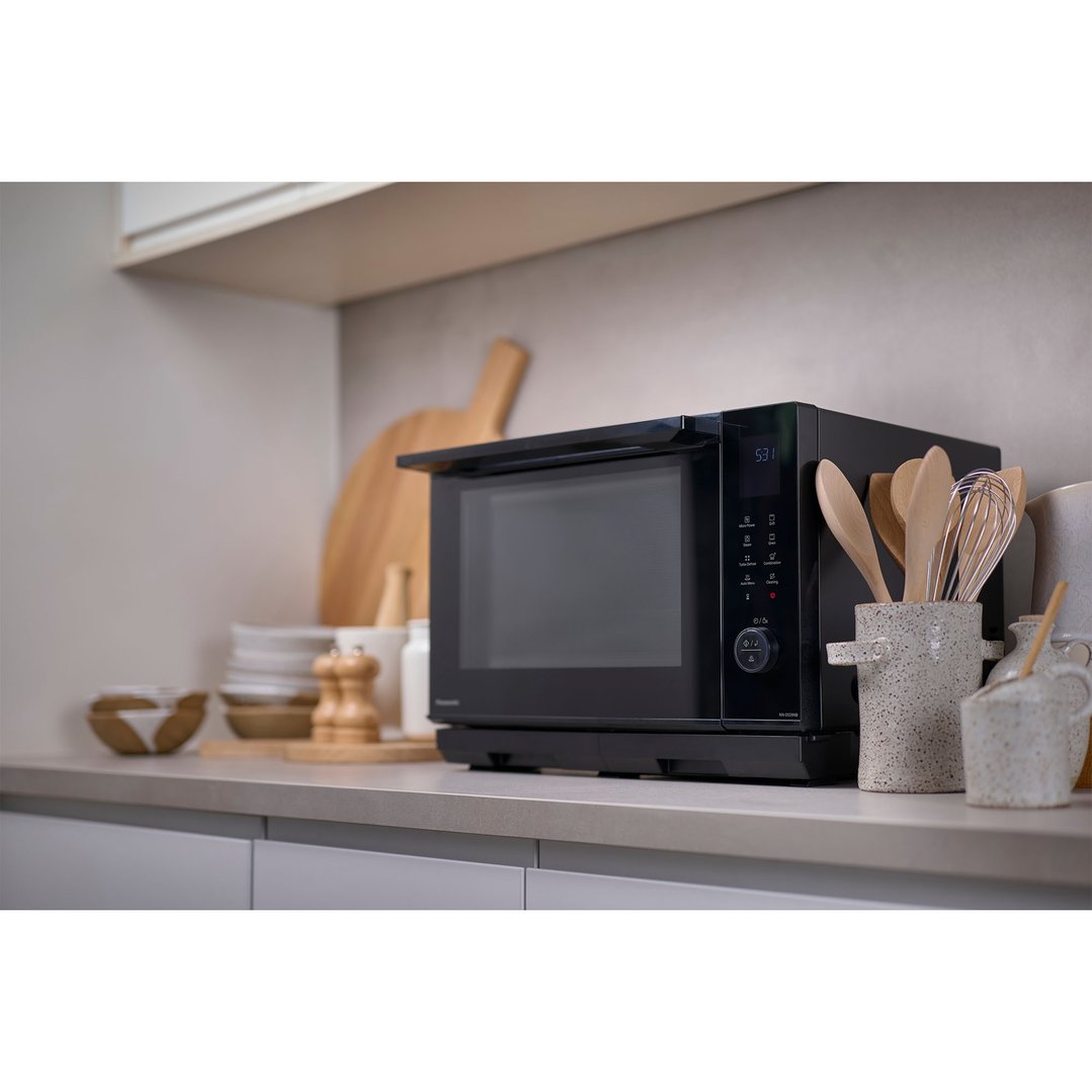 Black Panasonic microwave oven on a kitchen counter with cooking utensils