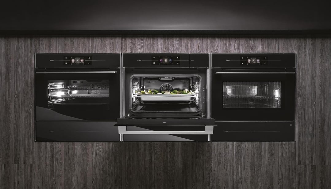Three built-in ovens in a dark wood kitchen, one open with food inside