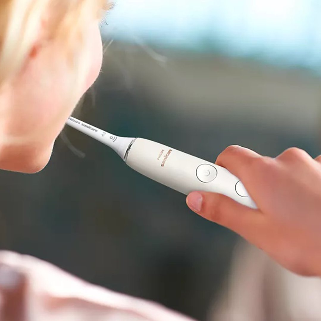 Person holding a white Philips Sonicare electric toothbrush to their mouth