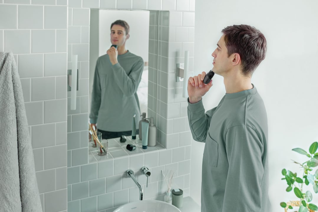 Man shaving with a compact shaver in front of a bathroom mirror