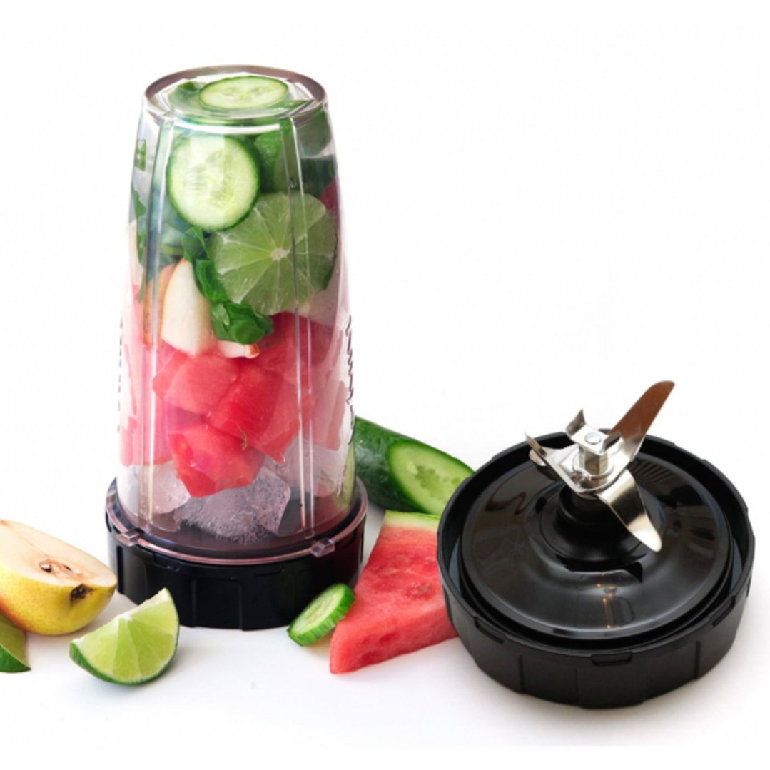 Blender cup filled with fruit and vegetables, with a blade attachment and fruit on a white surface