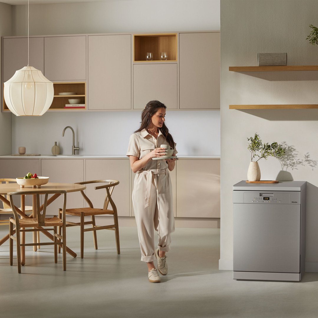 Woman holding dishes in a modern kitchen with a freestanding dishwasher