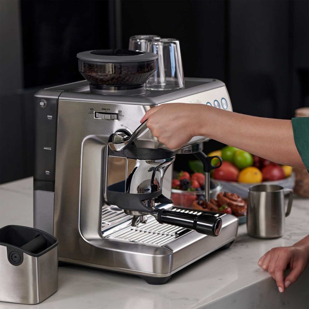 Hand operating a Breville coffee machine with coffee beans and cups