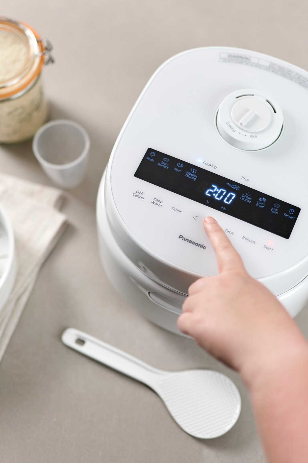 Hand adjusting settings on a white Panasonic rice and multi cooker
