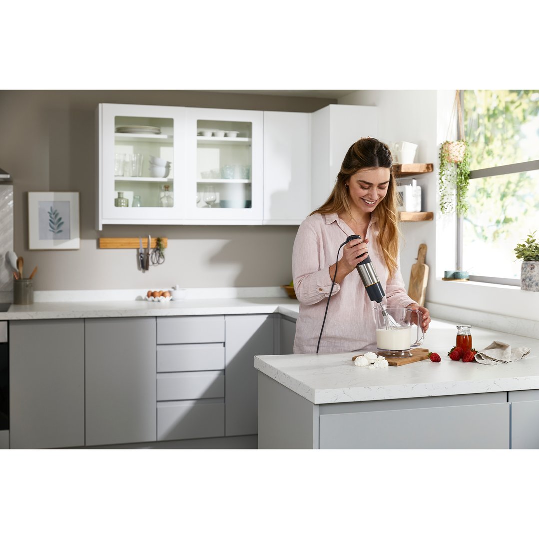 Woman using a KENWOOD stick blender to whisk milk in a modern kitchen