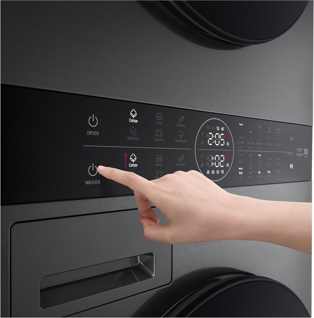 Hand pressing the washer power button on a black stacked washer dryer