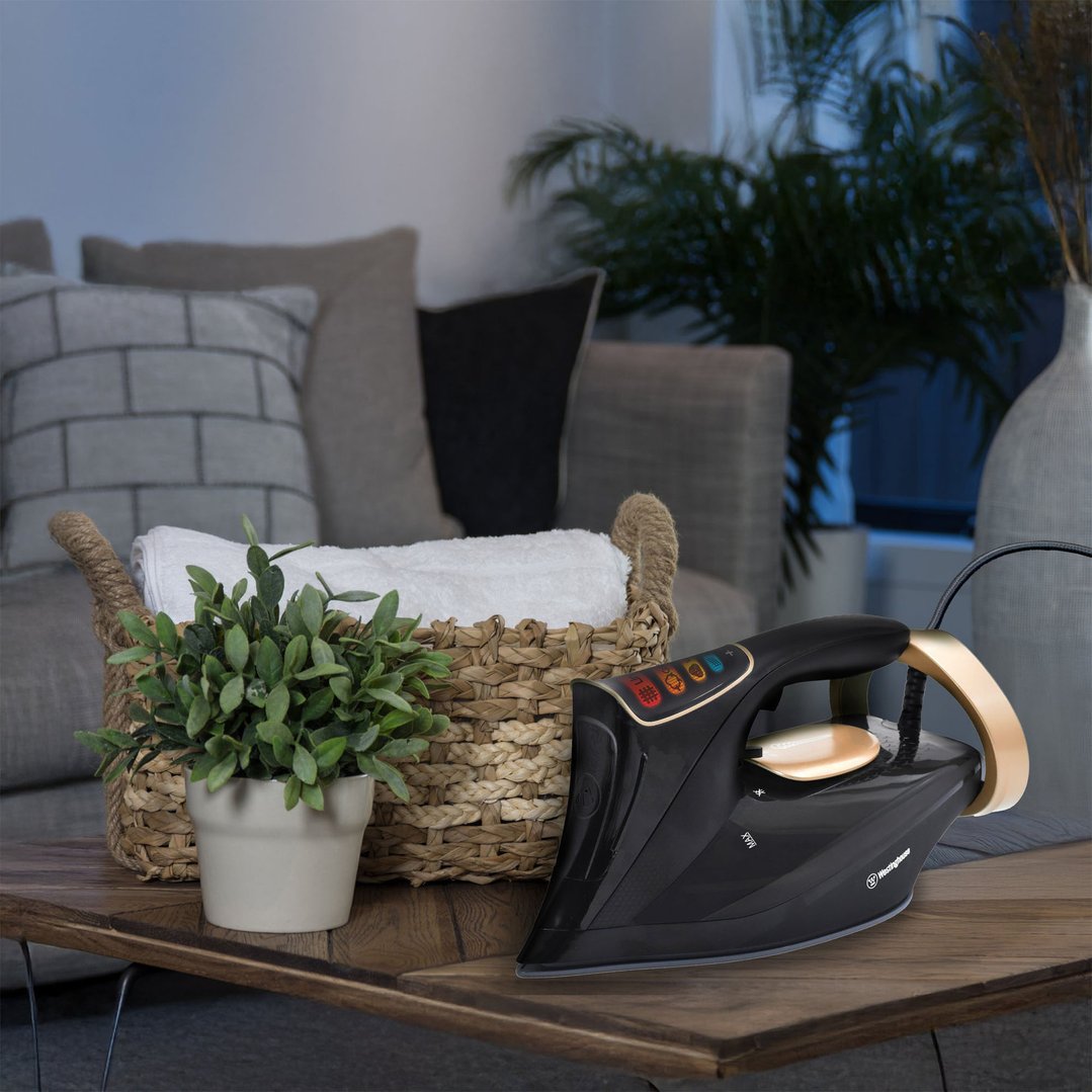 Black and gold steam iron on a wooden table with a plant and basket