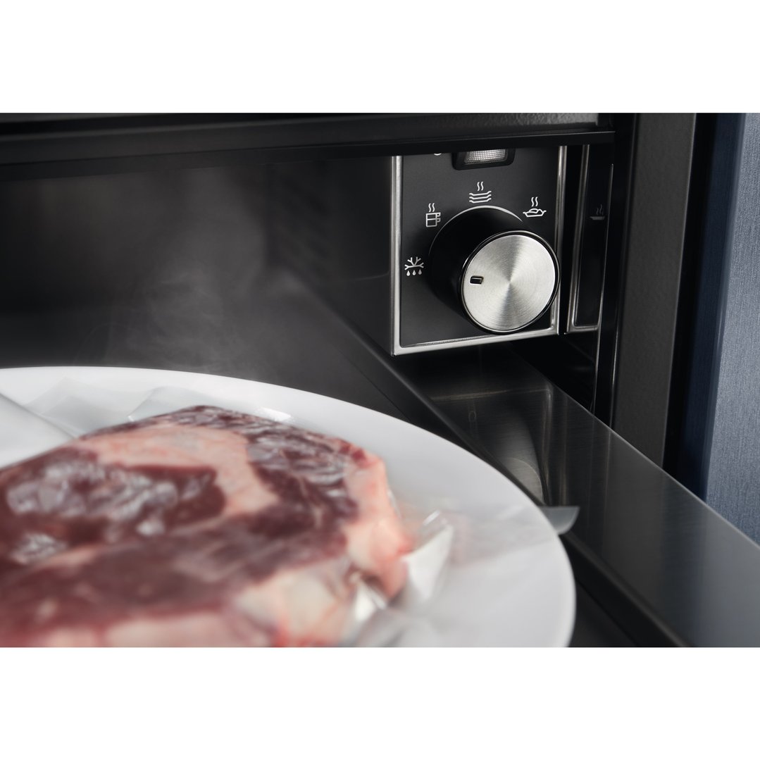 Close up of a warming drawer with a steak on a plate inside