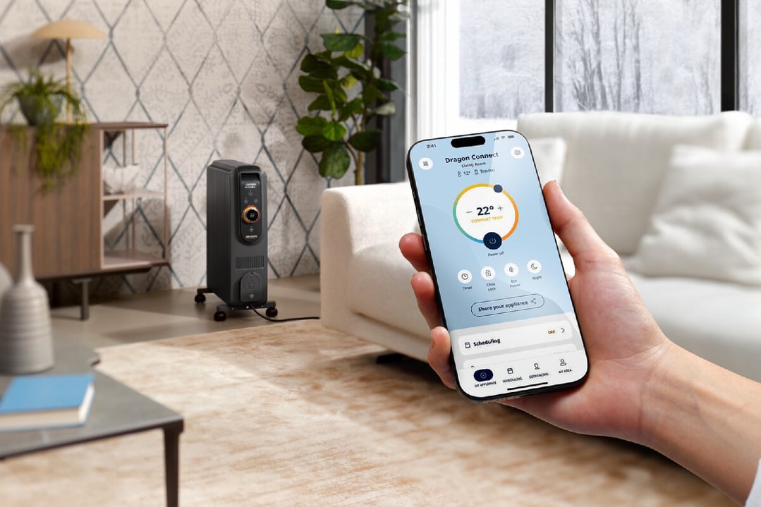Hand holding a smartphone controlling a DeLonghi oil column heater in a living room