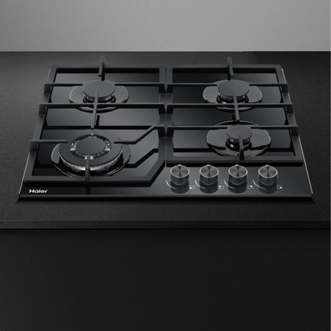 Black gas on glass cooktop with four burners and control knobs on a dark countertop