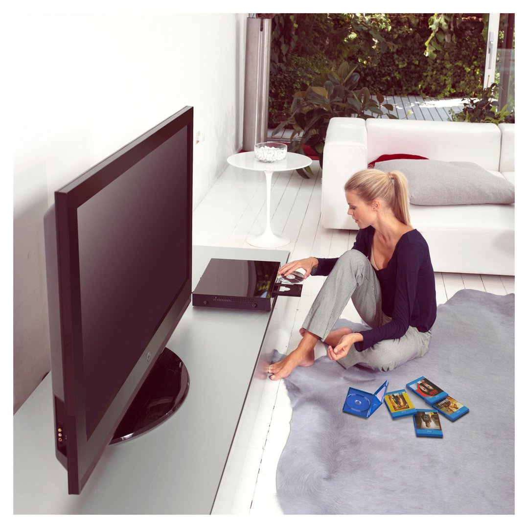 Woman inserting a disc into a Blu-Ray player next to a TV