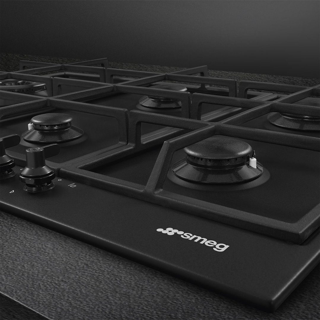 Close up of a matte black gas cooktop with grates and controls